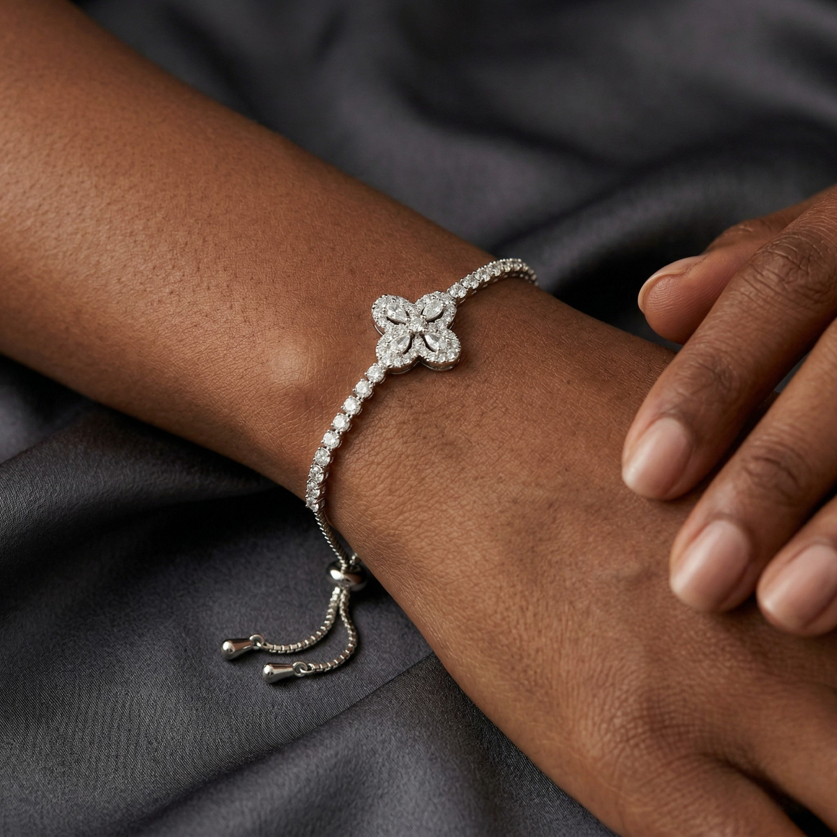 Silver bracelet with floral design on a wrist against a dark fabric background