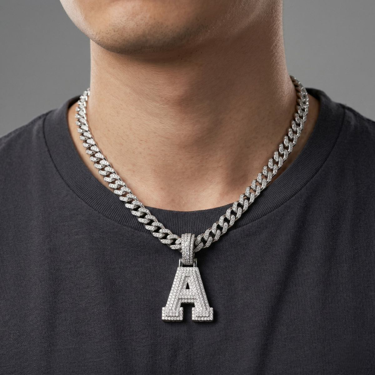 Man wearing a silver chain necklace with an 'A' pendant on a gray background