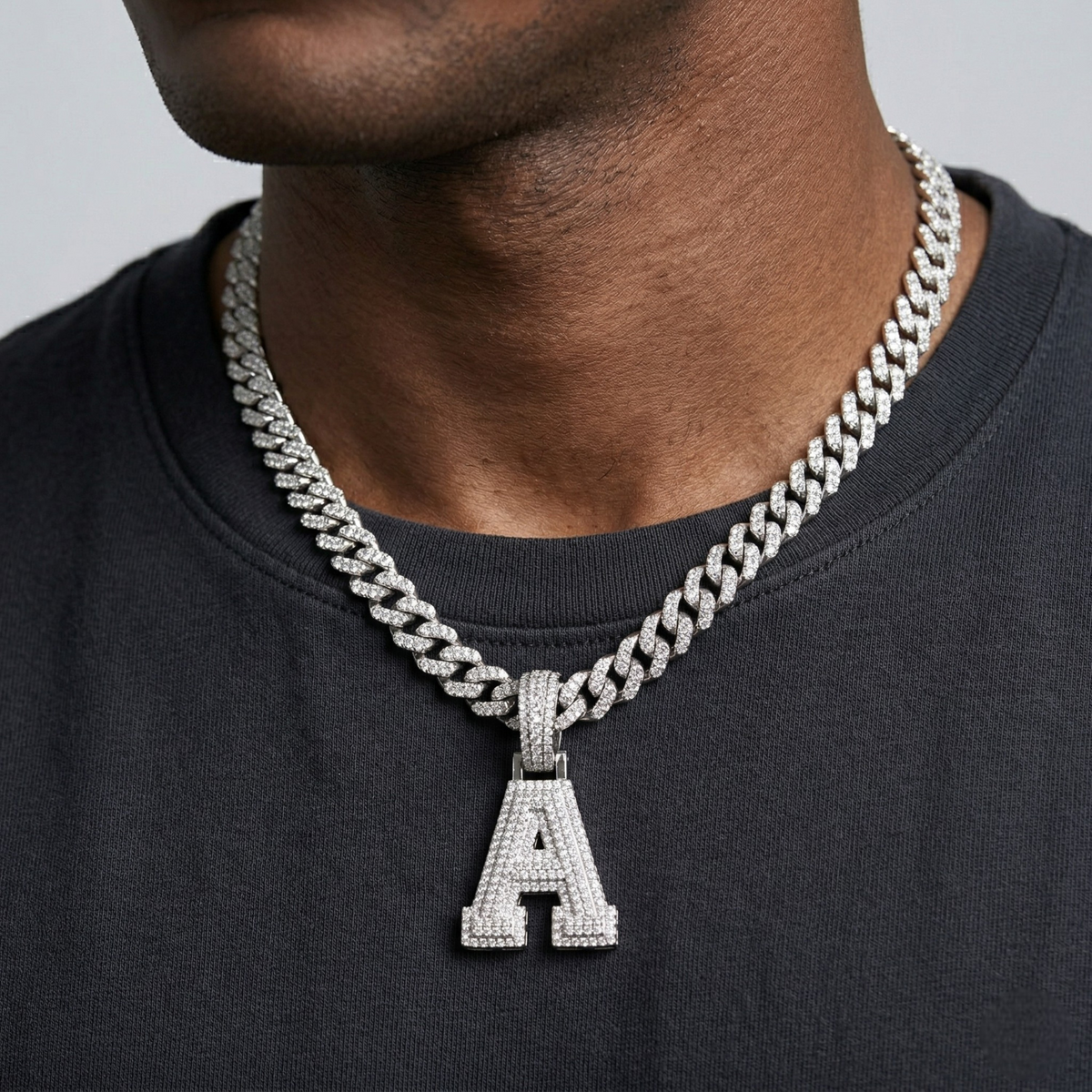 Person wearing a silver chain necklace with an 'A' pendant on a plain background