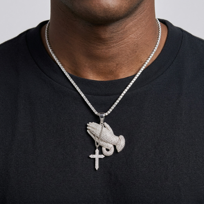 Person wearing a black shirt with a silver necklace featuring a hand and cross pendant.
