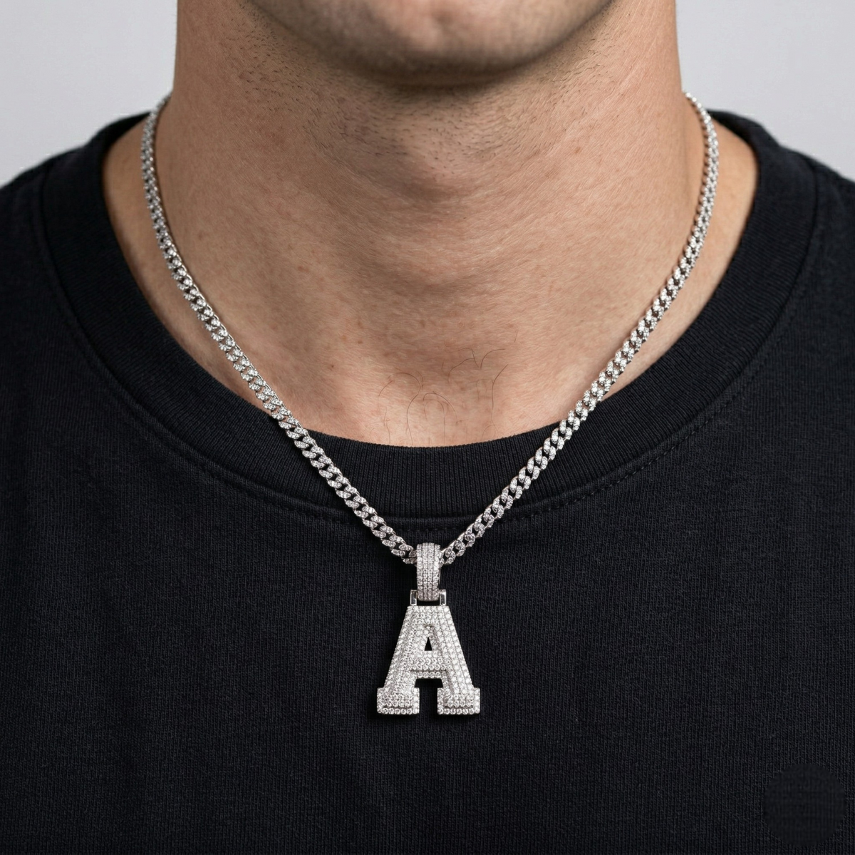 Person wearing a silver necklace with an 'A' pendant on a plain background