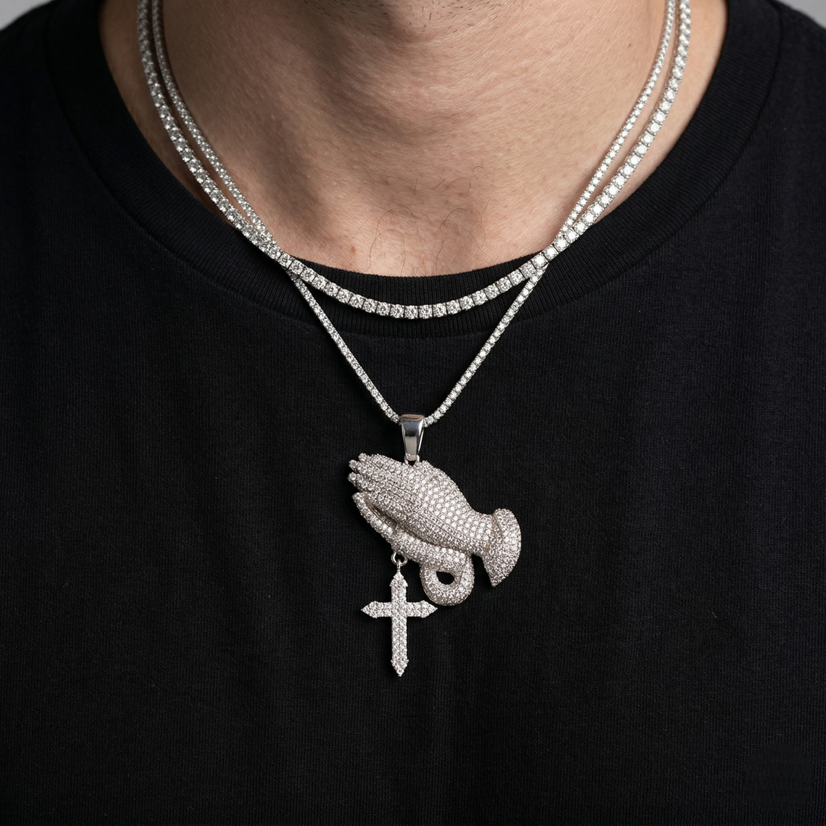 Close-up of a person wearing a silver necklace with a praying hands pendant on a black background